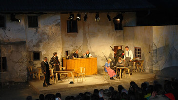 Theateraufführung im Freien mit historischer Kulisse und Publikum in der Abenddämmerung.