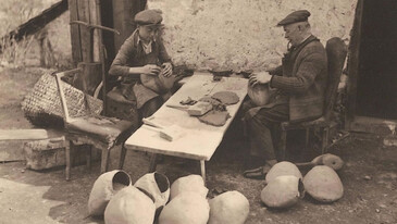 Zwei Männer beim traditionellen Schellenschmieden im Freien mit fertigen Produkten am Boden.