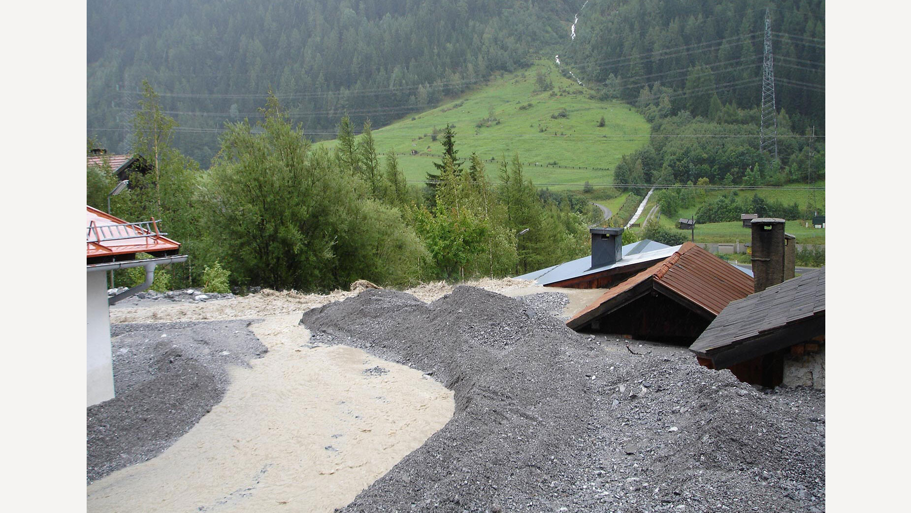 Geröll und Schlamm liegen meterhoch auf Dächern nach Murereignis / Debris and mud piled high on rooftops after mudslide event