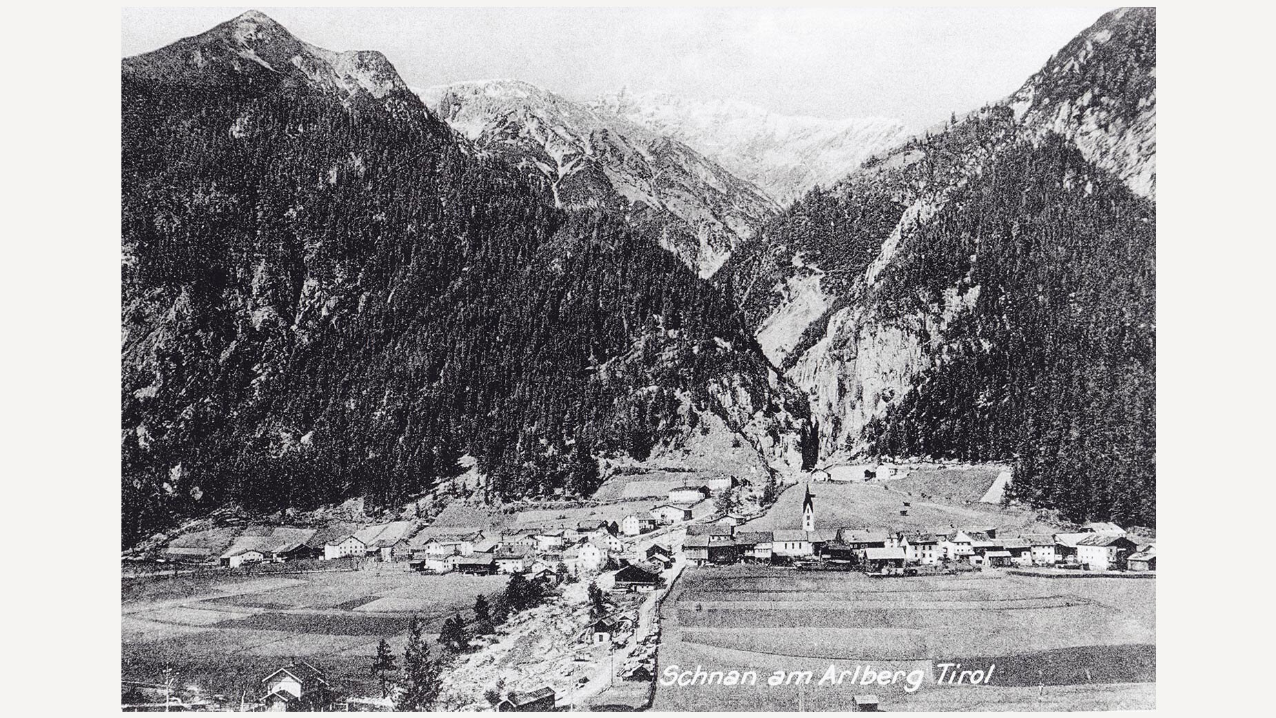 Historische Schwarzweißaufnahme eines Dorfes im Tal zwischen bewaldeten Bergen / Historic black-and-white photo of village in valley between forested mountains