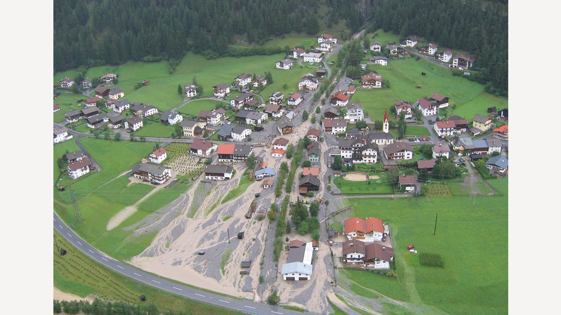 Luftaufnahme eines Dorfes mit durch Mure beschädigtem Bereich im Zentrum / Aerial view of village with mudslide-affected area in the center