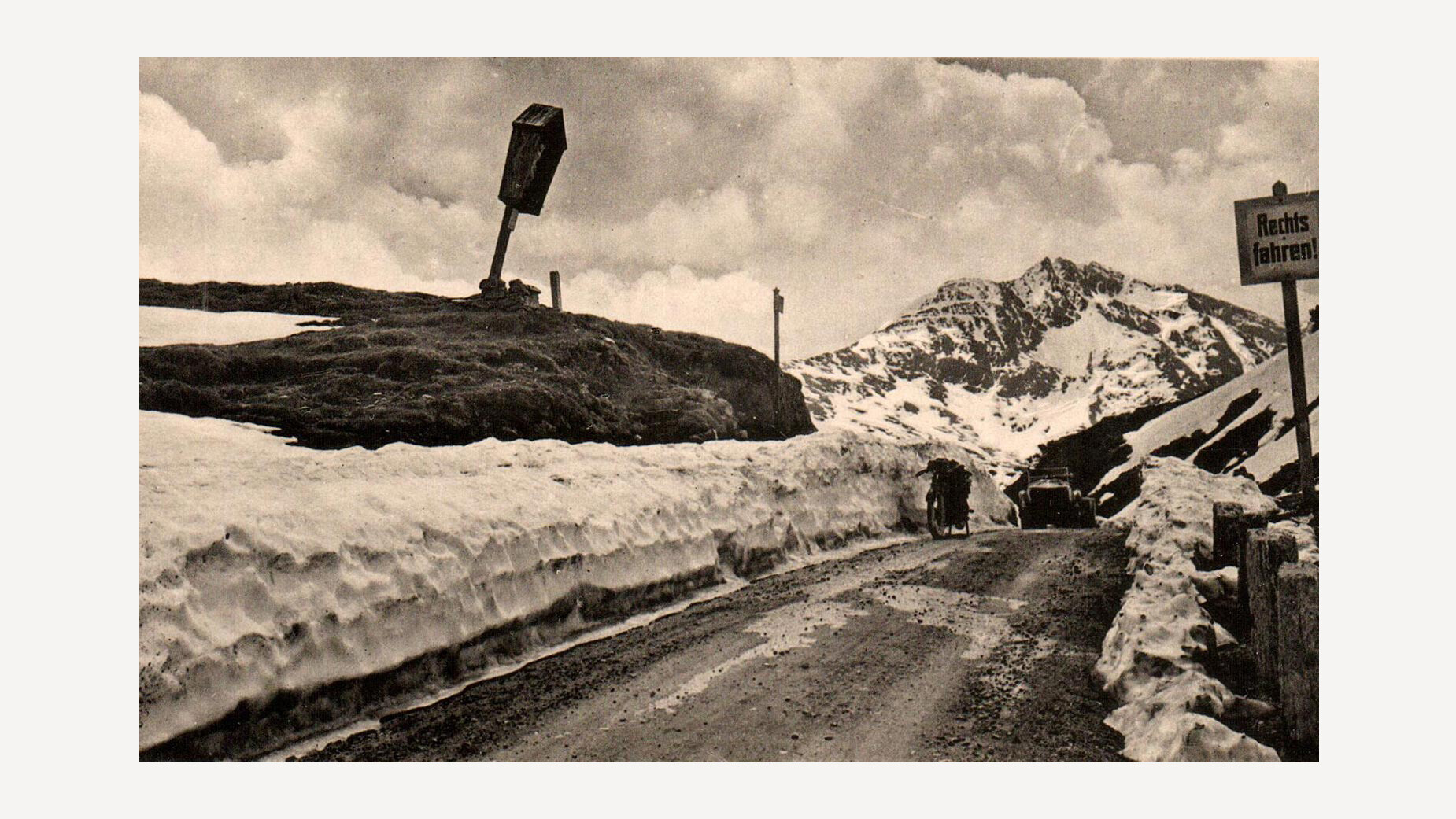 Freigeräumte Straße über den verschneiten Arlbergpass mit hohen Schneewänden und Verkehrsschild / Cleared road over the snow-covered Arlberg pass with high snow walls and traffic sign