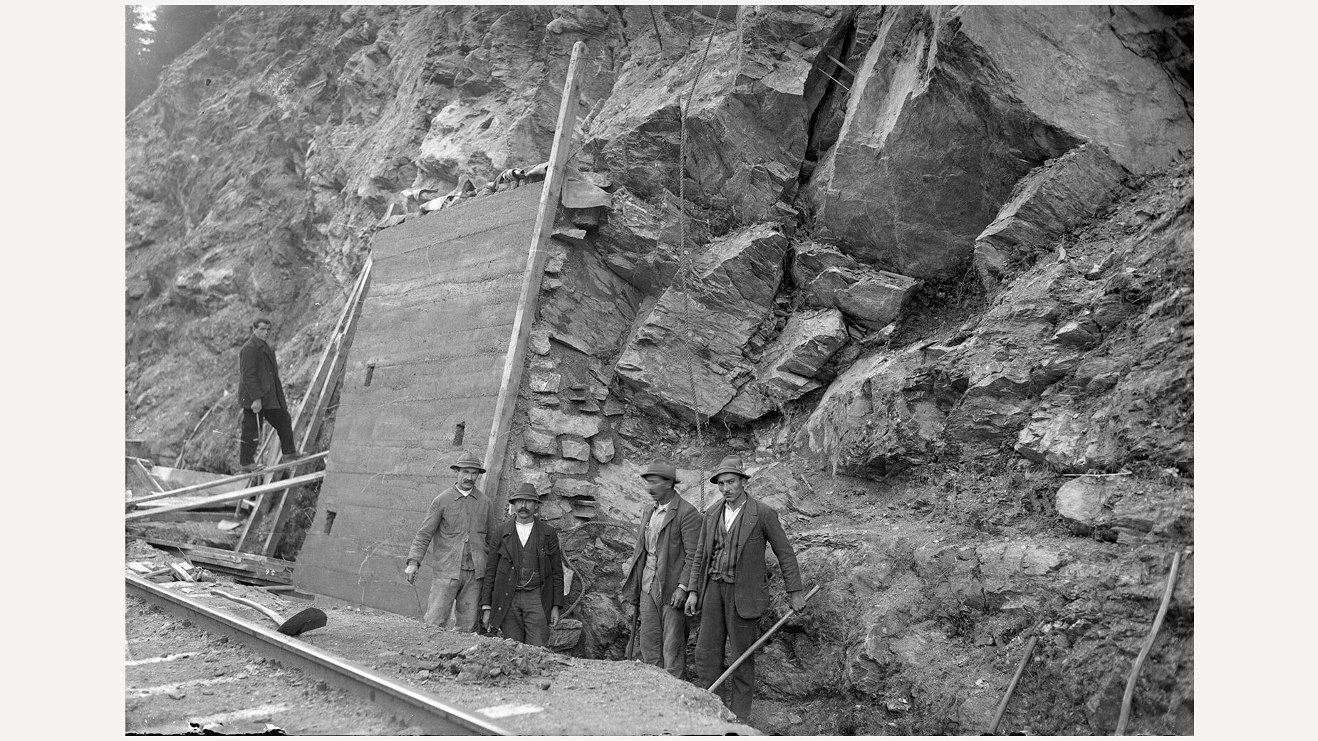 Historische Szene mit Männern vor einem Erdrutsch, umgeben von Gesteinsbrocken und Hangabsicherung / Historical scene showing men in front of a landslide, surrounded by rocks and slope reinforcements