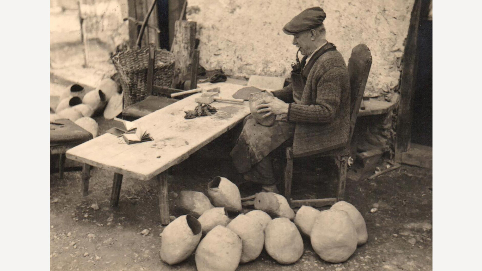 Mann schnitzt mit Messer an Tisch vor mehreren Kuhschellen / Man carving with knife at table in front of several cowbells