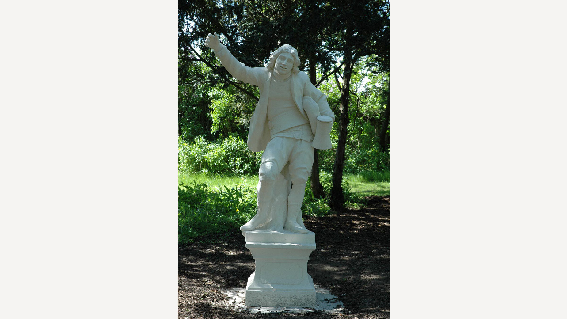 Tiroler Hiasl Denkmal / Tyrolean Hiasl Monument Steinerne Statue eines Mannes mit erhobenem Arm in einem schattigen Park / Stone statue of a man with raised arm in a shaded park