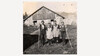 Schwarzweißbild von vier jungen Menschen in traditioneller Kleidung vor einer Alm mit Werkzeugen / Black-and-white photo of four young people in traditional clothing in front of an alpine hut with tools