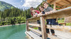 Familie lehnt sich über ein Holzgeländer an einem alpinen See mit klar grünem Wasser / Family leans over a wooden railing by an alpine lake with clear green water