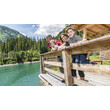 Familie lehnt sich über ein Holzgeländer an einem alpinen See mit klar grünem Wasser / Family leans over a wooden railing by an alpine lake with clear green water