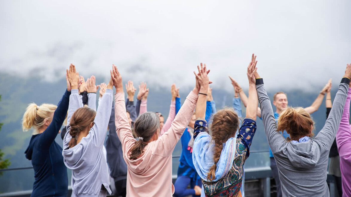 Gruppe Menschen streckt bei Outdoor-Yoga die Hände gemeinsam nach oben / Group of people raises their hands together during outdoor yoga