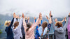 Gruppe Menschen streckt bei Outdoor-Yoga die Hände gemeinsam nach oben / Group of people raises their hands together during outdoor yoga