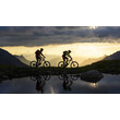 Zwei Mountainbiker fahren bei Sonnenuntergang auf einem Bergweg entlang eines stillen Sees / Two mountain bikers ride along a mountain trail by a calm lake at sunset
