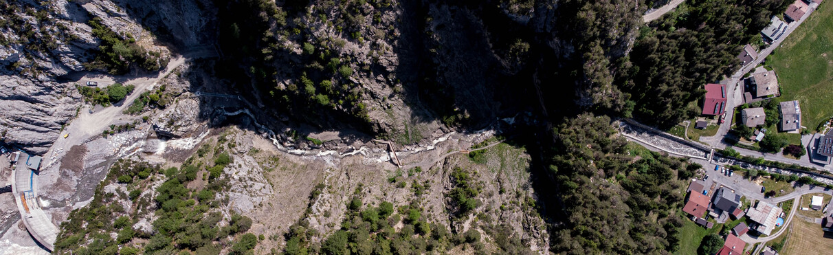 Aerial view of Schnanner Gorge with stream, bridges and paths. On the right are houses on the edge of the forest, on the left rocky slopes and a barrage.